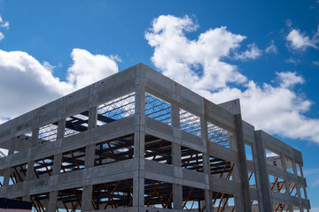 Multiple story precast grey concrete building with steel beams. The industrial structure in the corner of a skyscraper building with prefabricated engineering formwork. The sky is in the background. - obrazy, fototapety, plakaty