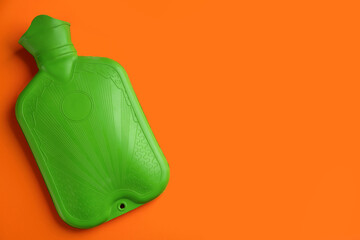 Green rubber hot water bottle on orange background, top view. Space for text