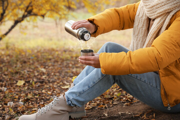 Fototapeta premium Woman with thermos sitting on ground outdoors, closeup