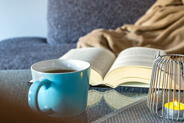 A thick book, a large blue mug of tea, a candle. Lazy winter weekend at home and reading a book.