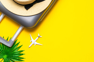 Suitcase, sunglasses with palm leaves and straw hat, white plane in travel composition on yellow background. Design of summer vacation holiday concept.