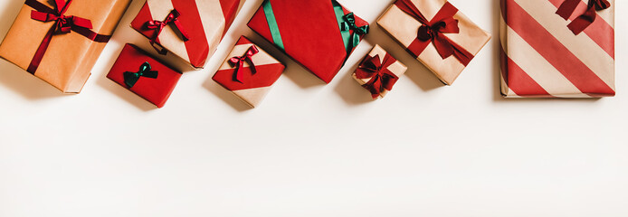 Fototapeta premium Flat-lay of festive craft gift boxes in wrapping paper decorated with colorful baubles, ribbons and bows over plain white background, top view, copy space. . Christmas boxing day concept