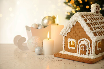 Beautiful gingerbread house decorated with icing and candles on white table