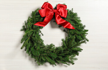 Christmas wreath made of fir branches with red bow on white wooden background © New Africa