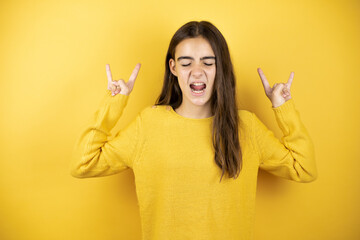 Pretty girl wearing a yellow sweater standing over isolated yellow background shouting with crazy...