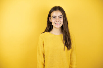 Fototapeta premium Pretty girl wearing a yellow sweater standing over isolated yellow background smiling