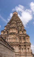 Hampi, Karnataka, India - November 4, 2013: Virupaksha Temple complex. South facade of east gopuram tower and entrance along wall under blue cloudscape.