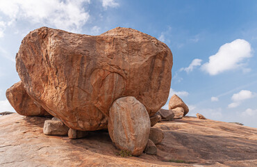 Hampi, Karnataka, India - November 4, 2013: Virupaksha Temple complex. Closeup of Huge brown boulders held by smaller ones above said temple under blue cloudscape.