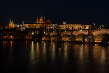 . prague castle and charles bridge and st. vita church lights from street lights are reflected on the surface of the vltava river in the center of prague at night in the czech republic