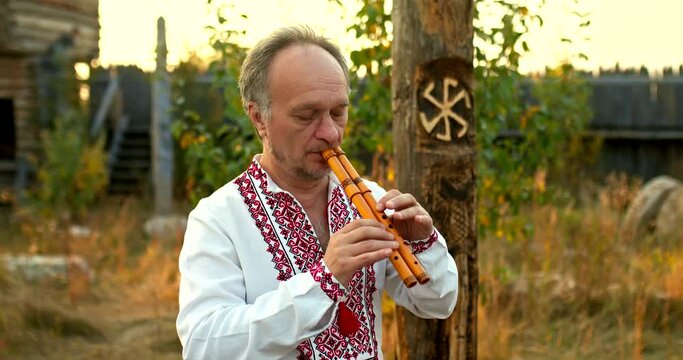 Folklore, a man in an embroidered national shirt plays the pipe with inspiration. Slavic customs of playing the pipe, ritual. Portrait view. 4k, ProRes