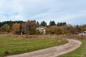 Scene of a Bulgarian village road poor broken cozy houses and vivid autumn trees in background hillside clousy overcast