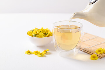 Organic Chrysanthemum flower tea in teapot and pouring into a cup  on white background, Healthy herbal drink