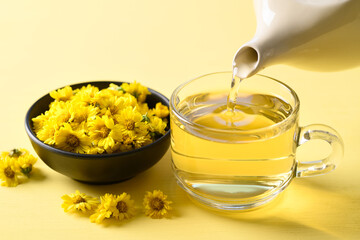 Organic Chrysanthemum flower tea in teapot and pouring into a cup  on yellow background, Healthy...