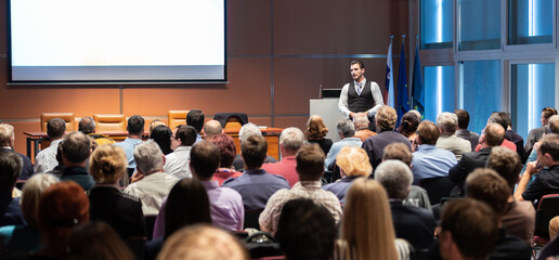 Speaker giving a talk in conference hall at business meeting event. Rear view of unrecognizable people in audience at the conference hall. Business and entrepreneurship concept.