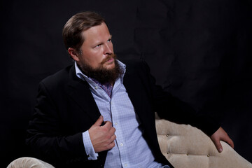 Thoughtful solid bearded man dressed in suit sitting on sofa