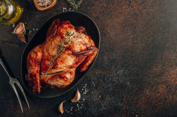 Homemade chicken roasted with thyme, garlic on a black board on a dark table.