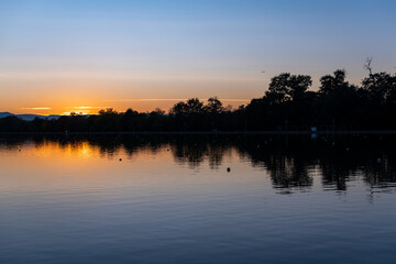 Sunset vibrant reflections in deep blue water symmetry silhouette landscape nature alley park shore forest island