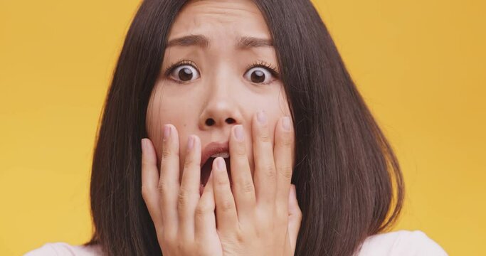 Close up portrait of young afraid asian lady, feeling afraid and panicked , orange studio background