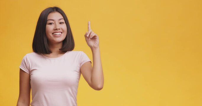 Excited asian woman having great idea, feeling inspiration, standing over orange studio background with free space