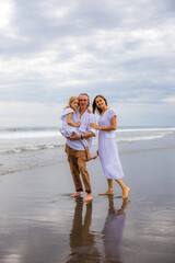 Happy family spending time at the beach. Summer holidays. Family vacation. Mother, father and daughter walking along the beach. Father carrying daughter in his arms. Copy space.