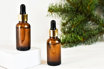 Two dropper oil bottles. Serum oil in glass bottles with a dropper with fir tree branches on a white background. Natural organic cosmetic, eco lotion, essence, serum. Copy space. Advertising.