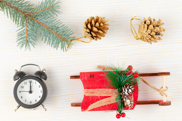Fototapeta na wymiar alarm clock, santa claus sleigh, golden fir-tree cone and branch on white wood background with gold veins