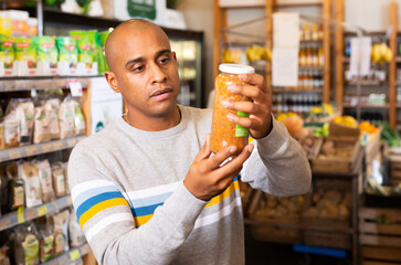 Latin american man reading jar contents on label while shopping in food department of supermarket
