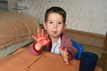 Two-three years old child painting with watercolors at home. Happy toddler boy with painted hand