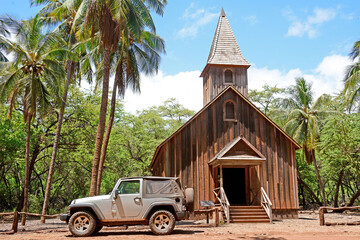 Driving offroad in rental car near an old historic wooden church surrounded by palm trees on Lanai...