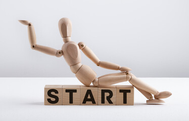 Wooden man sits on wooden cubes with the text START. Business Concept.