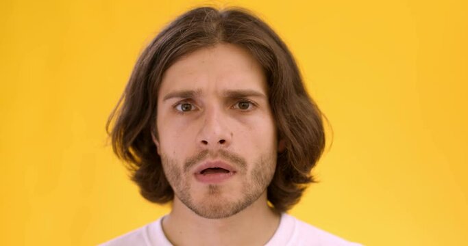 Close up shot of young amazed man thinking about idea, but rejecting it, shaking head no, orange studio background