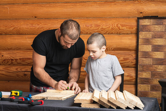 Father and son together make a wooden birdhouse in the workshop. Cheerful father with a little boy draws what kind of birdhouse they will have on a wooden table in the workshop