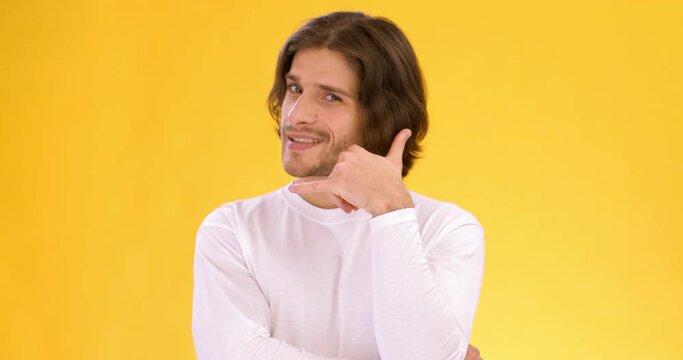 Young playful guy pointing at camera and showing phone gesture, flirting with you over orange studio background