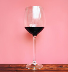 A large glass with red wine stands on a wooden table on a pink background. Isolate, copy space, foreshortening and bottom view.