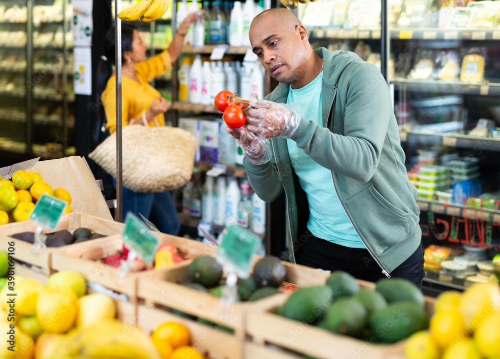 Wall mural man shopper chooses ripe tomatoes at grocery supermarket