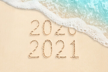 2020 and 2021 handwritten numbers on sand, beach and ocean wave on background