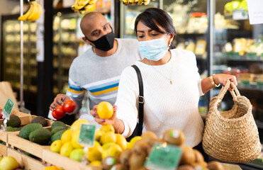 Man and woman in protective mask picking ripe tomatoes together at grocery store