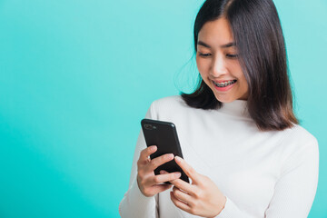 Portrait of Asian woman smile she holding and typing text message on a smartphone, female excited cheerful her reading mobile phone some social media isolated on a blue background, Technology concept
