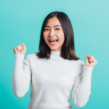 Young beautiful Asian woman cheerful surprised and amazed for success with arms raised, Portrait happy female glad-hands arms fists raised great big win competition, isolated on a blue background