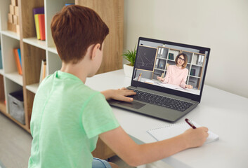 Boy pupil sitting at home and making notes during online lesson