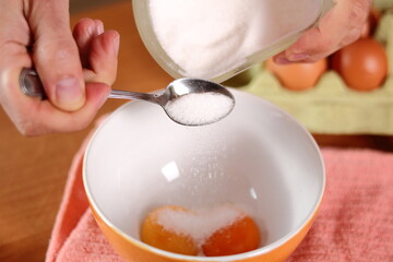 Adding sugar into bowl with egg yolks. Making mayonnaise with a wooden spoon.