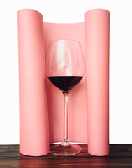 A large glass with red wine stands on a wooden table on a pink roll paper background. Isolate and copy space, menu, wine list concept.