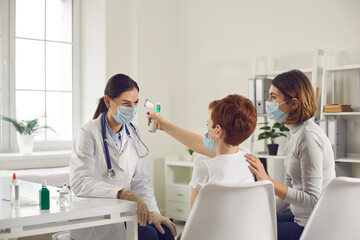 Obraz premium Little boy having fun at the hospital and measuring doctor's temperature with gun thermometer