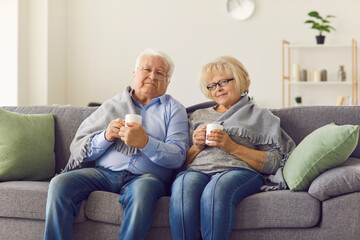Portrait of a senior couple wrapped in a plaid sitting on the couch and drinking hot tea.