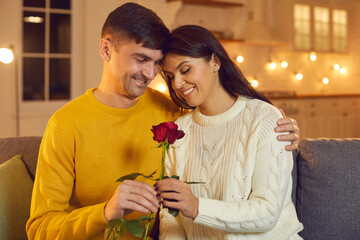 Husband tenderly embraces his wife giving her a red rose which is a symbol of their love.