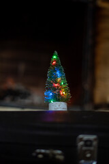 Fototapeta na wymiar small Christmas tree with lights near a stone fireplace with burning wood. cozy house, waiting for Christmas.