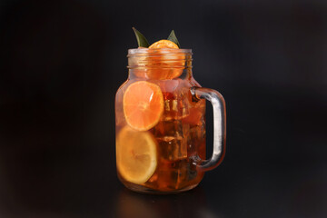 Liquid ice lemon orange tea with slice green leaf cinnamon stick in transparent glass jar mug on...