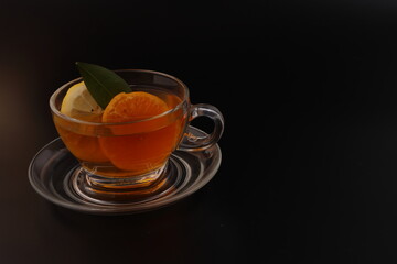 Obraz na płótnie Canvas Liquid tea lemon orange slice green leaf cinnamon stick in transparent glass teacup saucer on black background