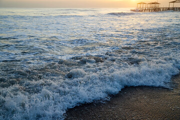 Naklejka premium Water of sea, waves with white foam, pierce and sky with sunset in a nice evening.
