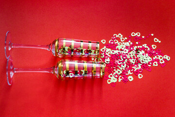 Glasses decorated with gold streamers on a bright background. Colorful hearts fall out of the glasses.